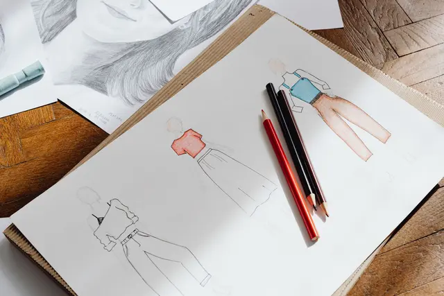 Fashion design sketches and colored pencils on a desk