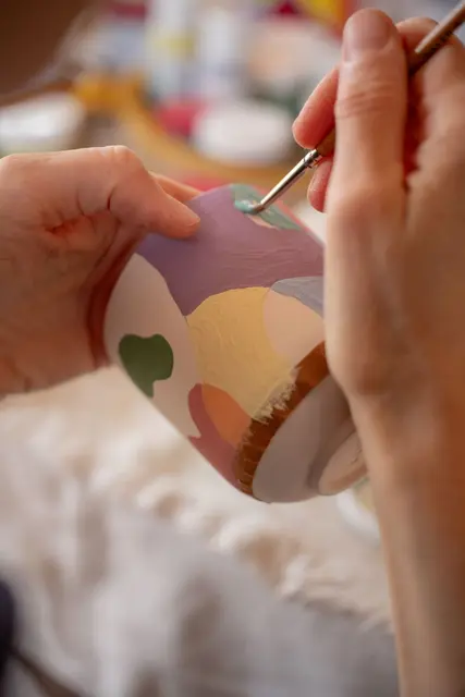 Hands painting a colourful ceramic mug at a pottery studio