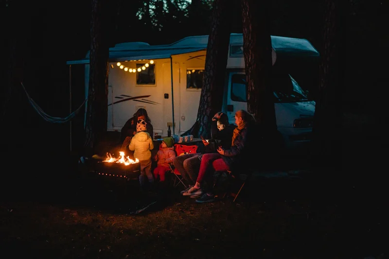 People around a campfire beside a campervan at night