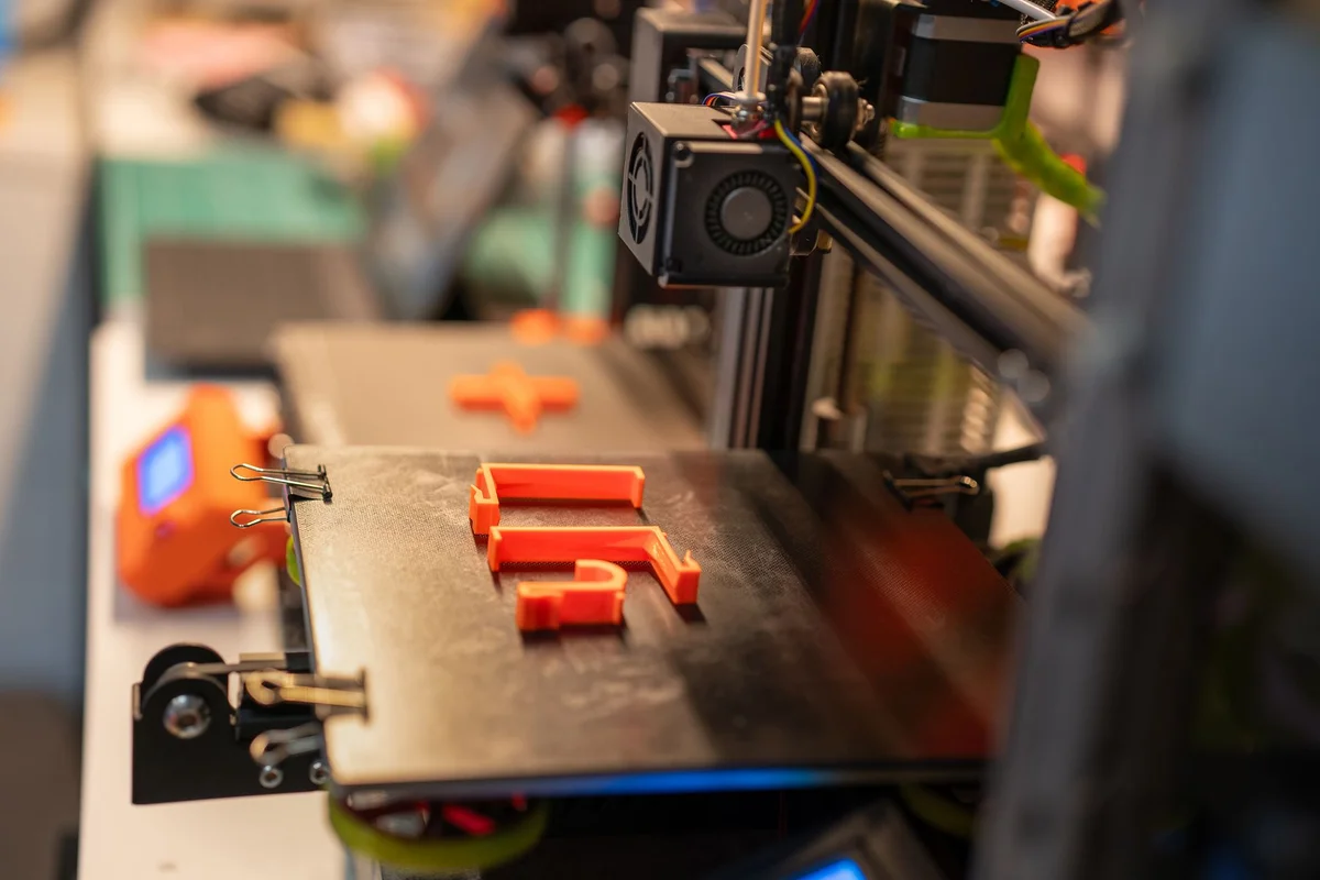 Close-up of a 3D printer building bright orange plastic parts on the print bed