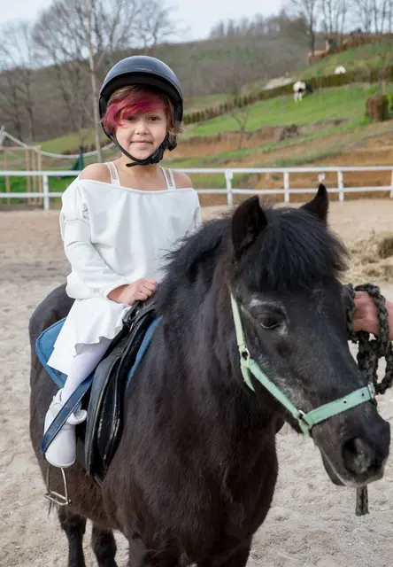 Girl in a riding helmet on a pony during a beginner lesson